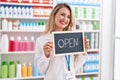 Young beautiful hispanic woman pharmacist smiling confident holding open blackboard at pharmacy