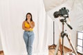 Young beautiful hispanic woman posing as model at photography studio looking confident at the camera smiling with crossed arms and Royalty Free Stock Photo