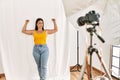 Young beautiful hispanic woman posing as model at photography studio showing arms muscles smiling proud Royalty Free Stock Photo