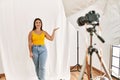 Young beautiful hispanic woman posing as model at photography studio smiling cheerful presenting and pointing with palm of hand Royalty Free Stock Photo