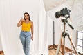 Young beautiful hispanic woman posing as model at photography studio smiling doing phone gesture with hand and fingers like Royalty Free Stock Photo