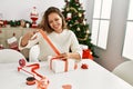 Young beautiful hispanic woman preparing christmas gift sitting on table at home Royalty Free Stock Photo