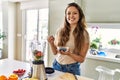 Young beautiful hispanic woman preparing vegetable smoothie with blender holding bowl with blueberries at the kitchen Royalty Free Stock Photo