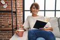 Young beautiful hispanic woman reading book and drinking coffee sitting on sofa at home Royalty Free Stock Photo