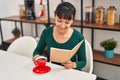 Young beautiful hispanic woman reading book and drinking coffee sitting on table at home Royalty Free Stock Photo