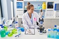 Young beautiful hispanic woman scientist writing report holding marijuana at laboratory