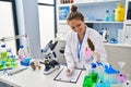 Young beautiful hispanic woman scientist writing report holding marijuana at laboratory