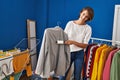 Young beautiful hispanic woman smiling confident cleaning jacket using pet hair roller at laundry room