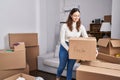 Young beautiful hispanic woman smiling confident holding fragile package at new home