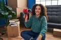 Young beautiful hispanic woman smiling confident holding package tape machine at new home