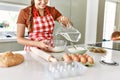 Young beautiful hispanic woman smiling confident pouring water on bowl with flour at the kitchen Royalty Free Stock Photo