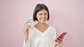 Young beautiful hispanic woman smiling holding dollars and smartphone over isolated pink background Royalty Free Stock Photo