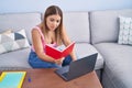 Young beautiful hispanic woman student sitting on sofa reading book at home Royalty Free Stock Photo