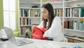 Young beautiful hispanic woman student using laptop holding book of backpack at university classroom Royalty Free Stock Photo