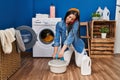 Young beautiful hispanic woman talking on smartphone cleaning floor at laundry room