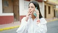 Young beautiful hispanic woman talking on the smartphone smoking cigarette at street