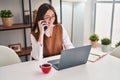 Young beautiful hispanic woman talking on smartphone using laptop at home Royalty Free Stock Photo