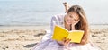 Young beautiful hispanic woman tourist reading book lying on sand at beach Royalty Free Stock Photo