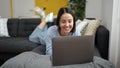 Young beautiful hispanic woman using laptop lying on sofa at home Royalty Free Stock Photo