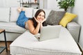 Young beautiful hispanic woman using laptop lying on sofa at home Royalty Free Stock Photo