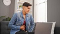 Young beautiful hispanic woman using laptop sitting on sofa suffering for stomachache at home Royalty Free Stock Photo