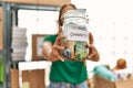 Young beautiful hispanic woman volunteer holding charity money jar at charity center