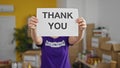 Young beautiful hispanic woman volunteer holding thank you message over face at charity center