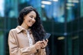 Young beautiful hispanic woman walking in the city, business woman holding phone in hands using smartphone app, woman Royalty Free Stock Photo