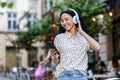 Young beautiful hispanic woman walks evening city in headphones, student listens to music online, uses an application on Royalty Free Stock Photo