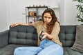 Young beautiful hispanic woman watching tv sitting on sofa with boring expression at home Royalty Free Stock Photo