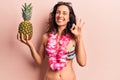 Young beautiful hispanic woman wearing bikini holding pineapple doing ok sign with fingers, smiling friendly gesturing excellent Royalty Free Stock Photo