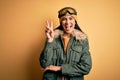 Young beautiful hispanic woman wearing ski glasses and coat for winter weather smiling with happy face winking at the camera doing Royalty Free Stock Photo