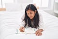 Young beautiful hispanic woman writing on notebook lying on bed at bedroom Royalty Free Stock Photo