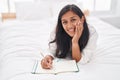 Young beautiful hispanic woman writing on notebook lying on bed at bedroom Royalty Free Stock Photo