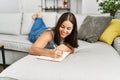 Young beautiful hispanic woman writing on notebook lying on sofa at home Royalty Free Stock Photo