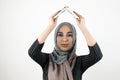 Young beautiful hopeful Muslim woman wearing turban hijab, headscarf holding book in her hands overhead isolated white Royalty Free Stock Photo