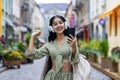 Young beautiful id woman walks in the city, tourist holds phone in hands, uses headphones to listen to music and online Royalty Free Stock Photo