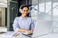 Young beautiful Indian female programmer working inside office with laptop, woman in headphones listening to audio