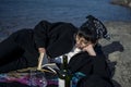 Young beautiful indian girl reading a book while leaning down on the ground wearing a black coat. Concept of having picnic in a Royalty Free Stock Photo