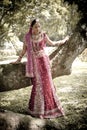 Young beautiful Indian Hindu bride standing under tree