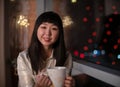A young, beautiful Korean Asian woman with a cup of tea in her cozy home with dreams of positive emotions in the evening Royalty Free Stock Photo