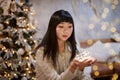 A young, beautiful Korean Asian woman holds a lighted festive garland in her cozy home with dreams of positive emotions