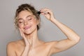 Young beautiful lady applying facial serum, using anti-aging treatment product, posing over grey studio background