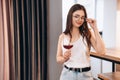 Young and beautiful lady in glasses is drinking red wine at home. Freestyle woman. Freelancer female relax