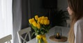 Young beautiful lady looks over bright bunch of yellow tulips on table. Romantic