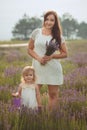 Young beautiful lady mother with lovely daughter walking on the lavender field on a weekend day in wonderful dresses and hats. Royalty Free Stock Photo