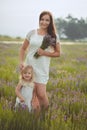 Young beautiful lady mother with lovely daughter walking on the lavender field on a weekend day in wonderful dresses and hats. Royalty Free Stock Photo