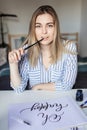 Young beautiful lady sitting at white desk and think about calligraphy Royalty Free Stock Photo