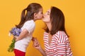 Young beautiful lady in striped shirt holds her daughter`s hand and kisses her. Little child with bouquet of flowers behinds back Royalty Free Stock Photo