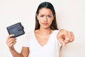 Young beautiful latin girl holding leather wallet pointing with finger to the camera and to you, confident gesture looking serious Royalty Free Stock Photo